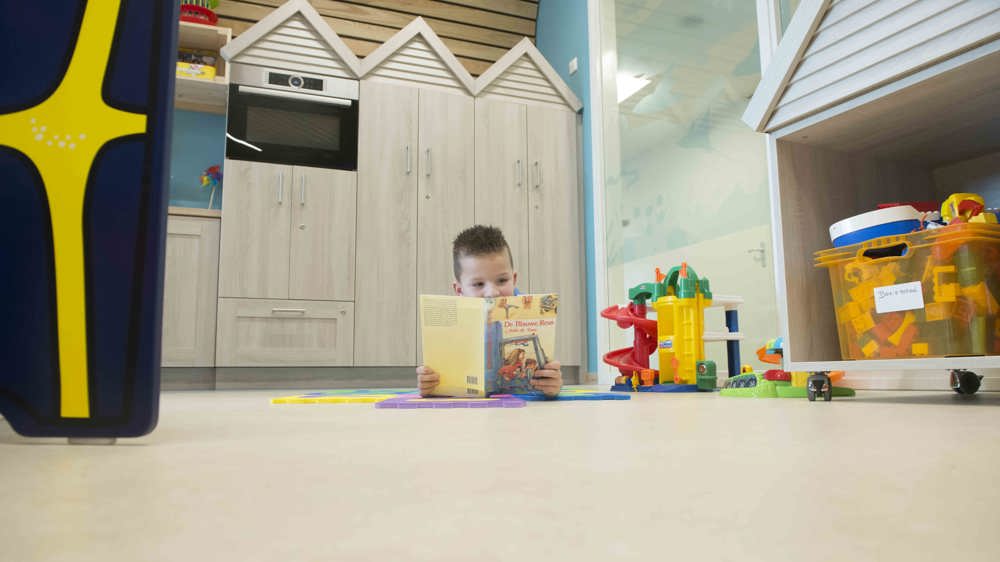 Kind leest boek in de speelkamer.