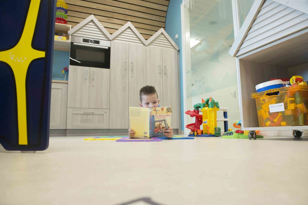 Kind leest boek in de speelkamer.