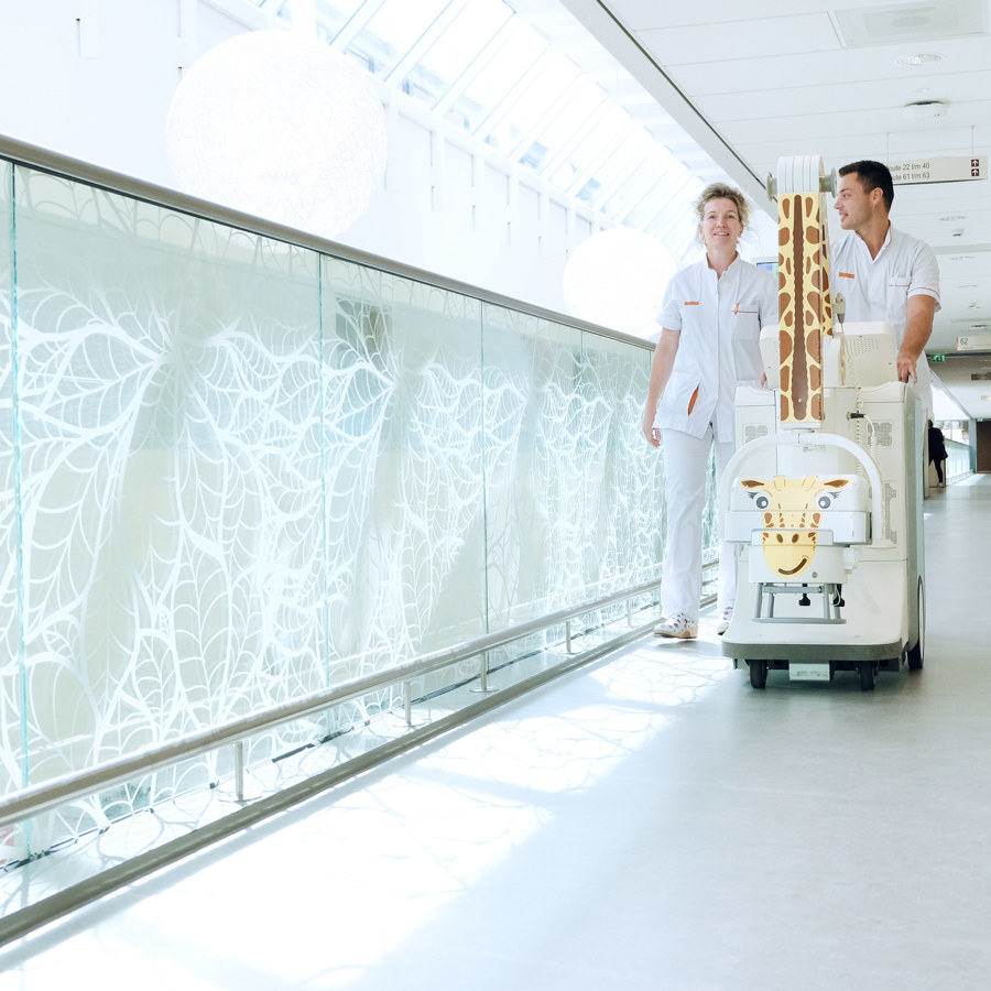 Twee medewerkers die achter een röntgen- apparaat lopen in een gang.